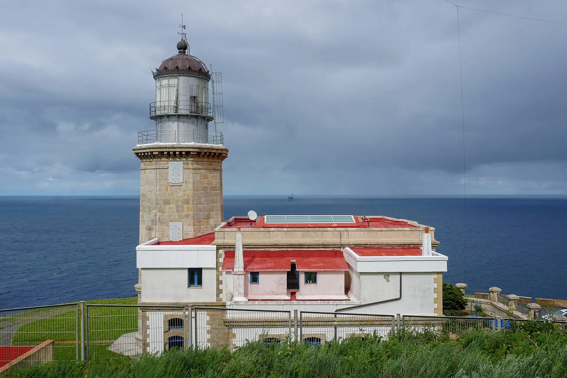 Faro de Matxitxako con su torre de piedra y edificios blancos de tejado rojo frente al mar