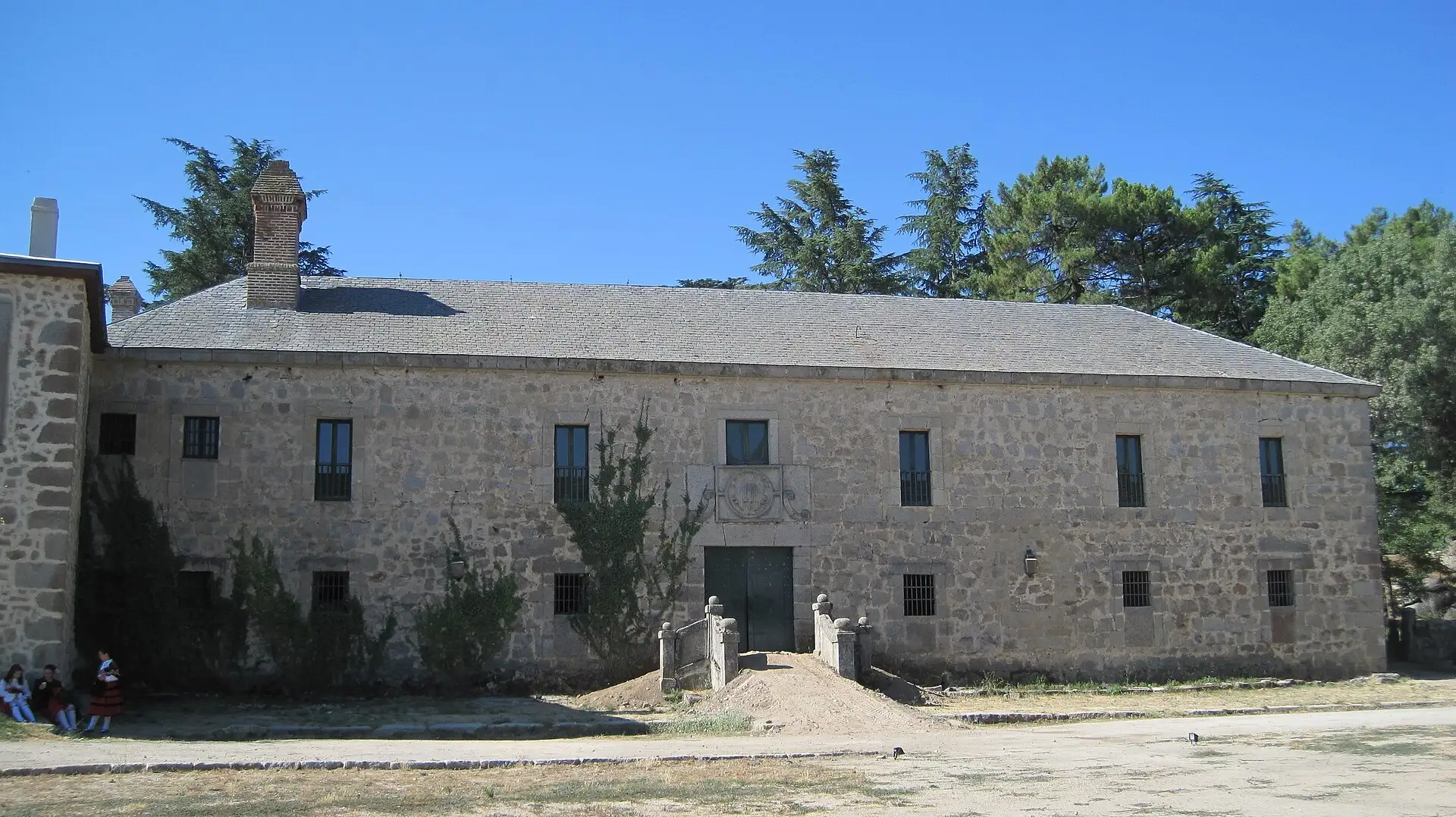 Edificio de piedra con tejado de pizarra de la finca La Granjilla, en El Escorial, rodeado de cedros