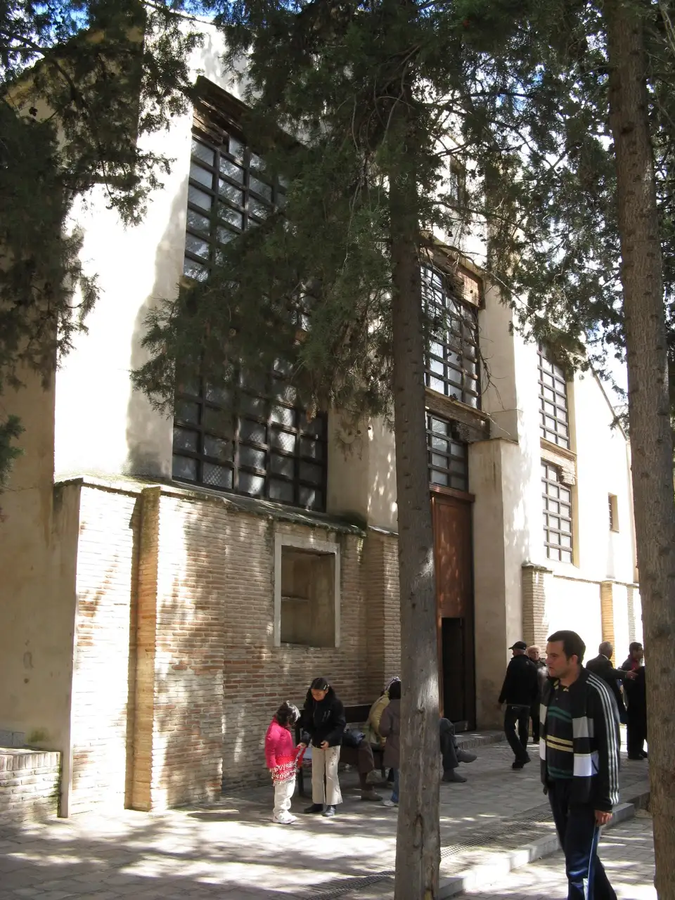 Fachada encalada y de ladrillo de la sinagoga de Santa María la Blanca entre cipreses, con visitantes en la entrada